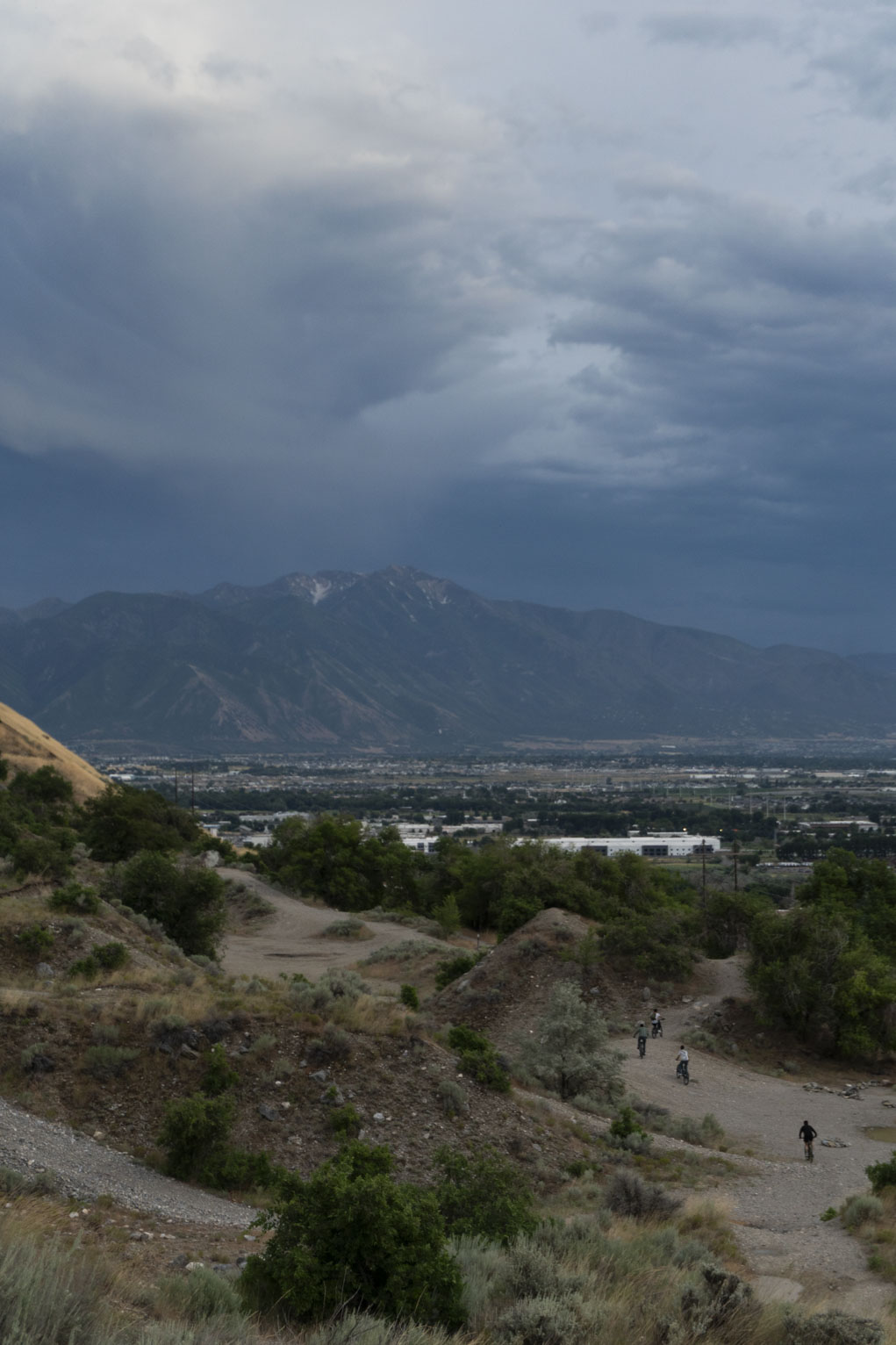 Some bikers ride on the mountainside, a town and shadowed mountains behind